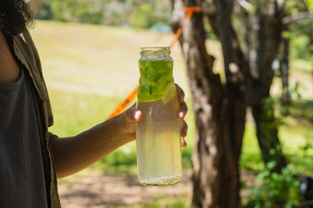 Mão de uma pessoa irreconhecível bebendo água fresca em uma garrafa de vidro, na floresta.