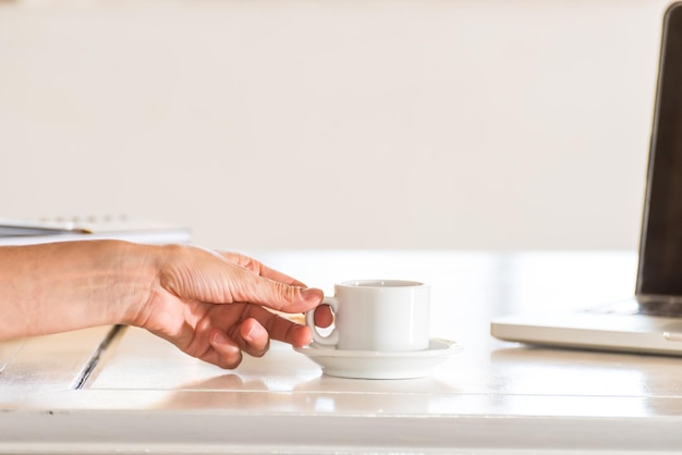 Mão delicada segurando uma caneca de café branca um computador portátil