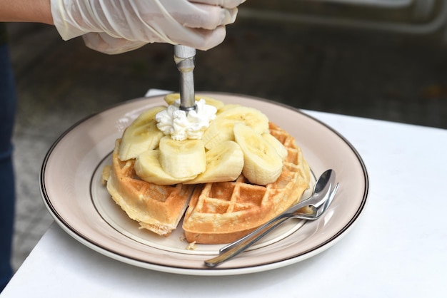 Mão derramando creme em waffles belgas com banana fatiada