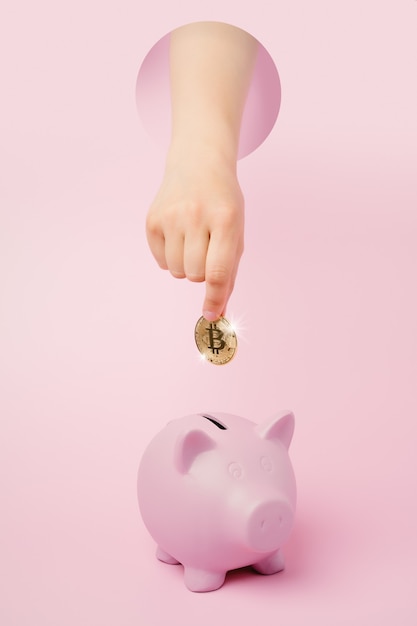 Foto mão desconhecida com um bitcoin dourado e um cofrinho rosa em um fundo economizando em criptomoeda