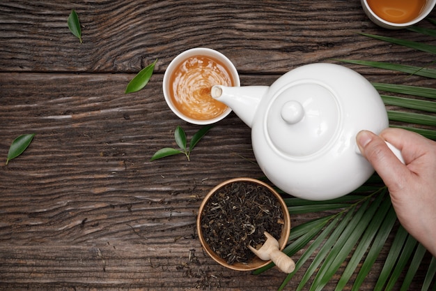 Foto mão despeje chá fumegante quente na xícara de bule e chá de ervas secas na mesa de madeira espaço vazio criativo plano leigos, produto orgânico da natureza para saudável com estilo tradicional