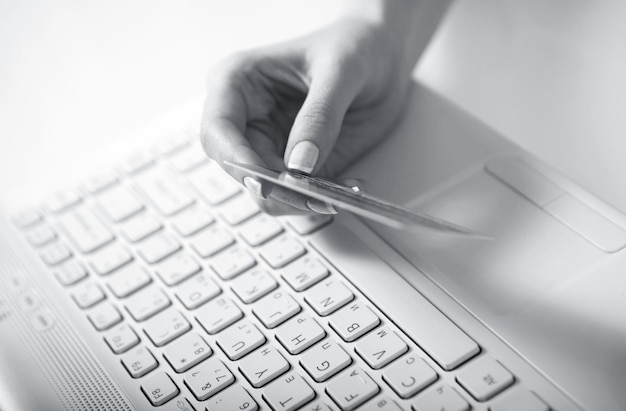 Mão direita de uma mulher segurando um cartão de crédito acima de um teclado se preparando para inserir dados