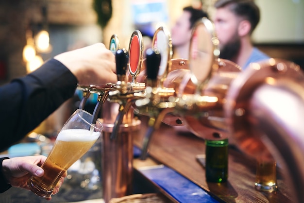 Mão do barman servindo ao cliente uma caneca de cerveja gelada