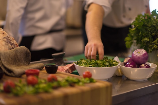 mão do chef servindo salada de legumes no prato na cozinha do restaurante