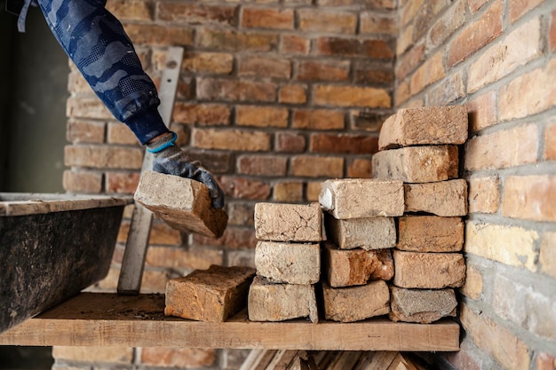 Mão do construtor tirando tijolos de uma pilha e fazendo uma casa