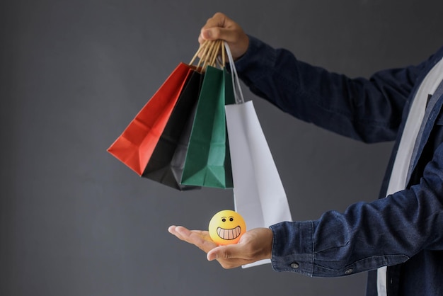 Mão do consumidor dando sacolas coloridas e emoticon feliz isolado em fundo cinza