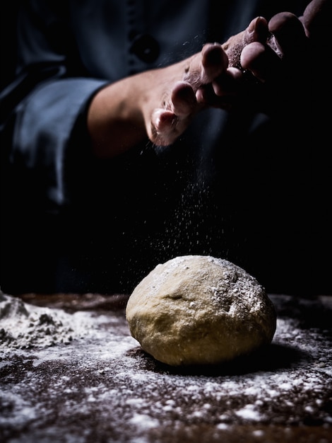 Mão do cozinheiro chefe de pastelaria que polvilha a farinha branca sobre a massa crua na mesa de cozinha.