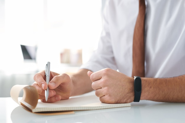 Mão do designer com caneta sobre a página em branco do bloco de notas enquanto faz um brainstorming antes de escrever ou desenhar