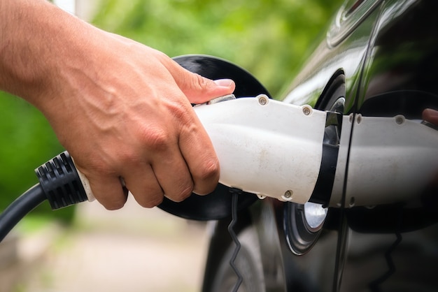 Mão do homem inserindo o plugue do carregador no carro elétrico em um ambiente verde