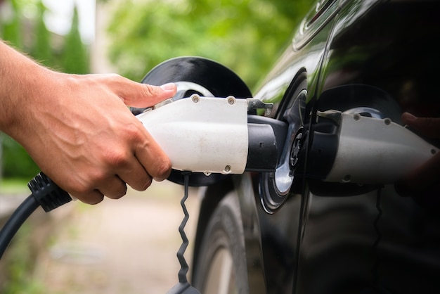 Mão do homem inserindo o plugue do carregador no carro elétrico