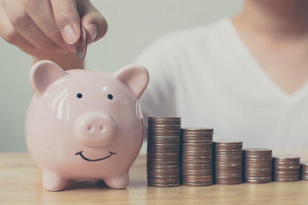 Foto mão do homem que põe moedas no mealheiro com dinheiro crescente da economia do crescimento da etapa da pilha do dinheiro. investimento de negócio de finanças de conceito