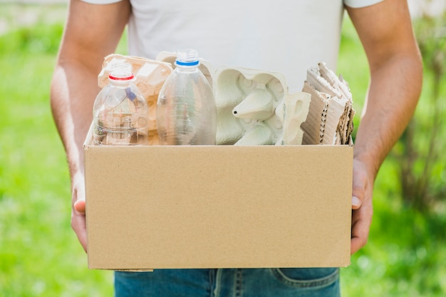 Mão do homem segurando produtos de reciclagem na caixa de papelão