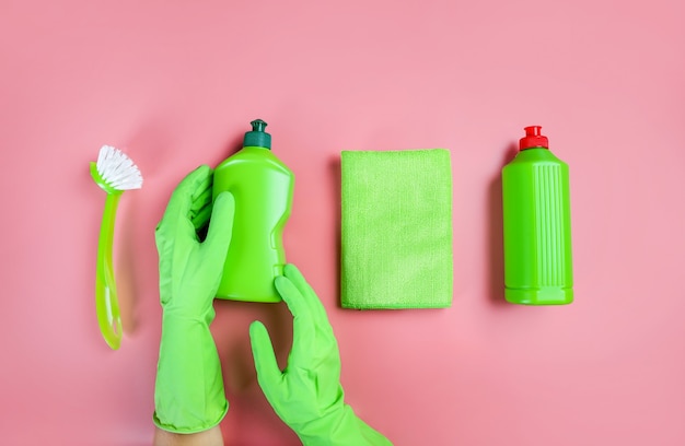 Mão do limpador segurando detergentes de limpeza no fundo rosa. Vista do topo