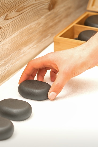 Foto mão do massagista com pedras de massagem na mesa do salão spa