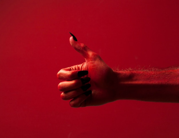 Mão do monstro do diabo vermelho de halloween com unhas pretas contra um fundo vermelho