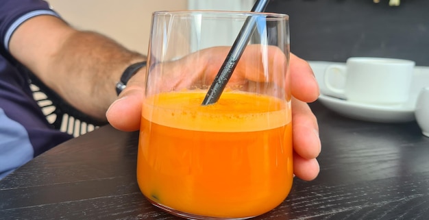 Mão e copo de vidro com suco de laranja ou cenoura