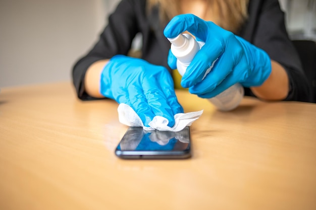 Foto mão em luvas azuis desinfetando limpeza smartphone telefone móvel na superfície da mesa de madeira com lenços molhados