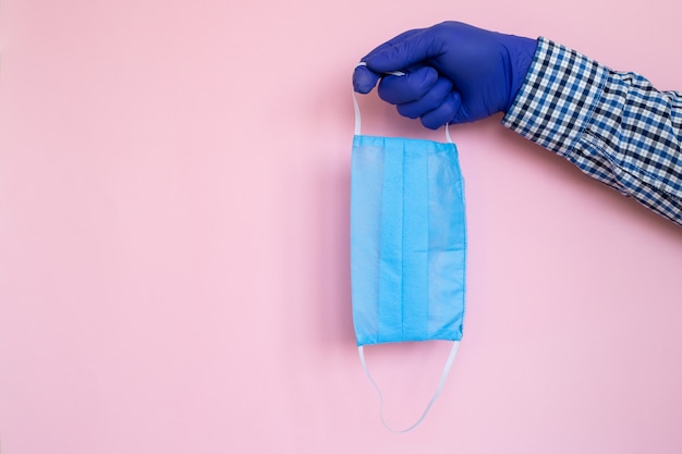 Foto mão em luvas médicas com máscara protetora isolada em fundo rosa. máscara para cobrir a boca e o nariz. conceito de proteção contra bactérias e vírus.