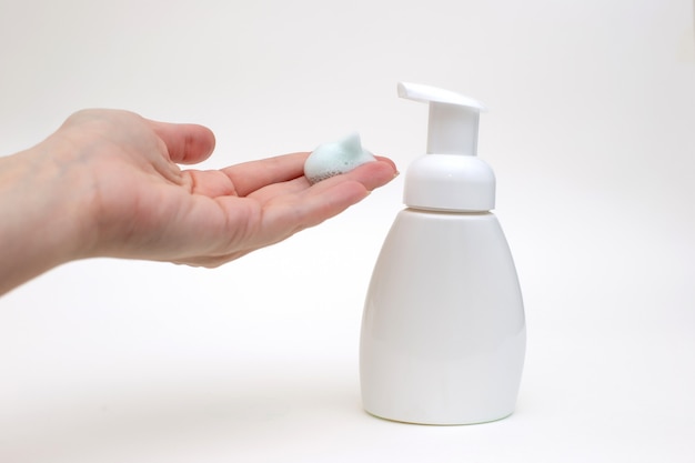 Mão em um fundo branco com espuma branca de uma garrafa de sabão antibacteriano