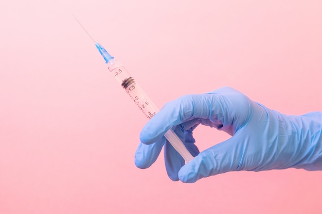 Mão em uma luva médica azul com uma seringa em um rosa. medicina, vacinação, saúde. minimalismo, .