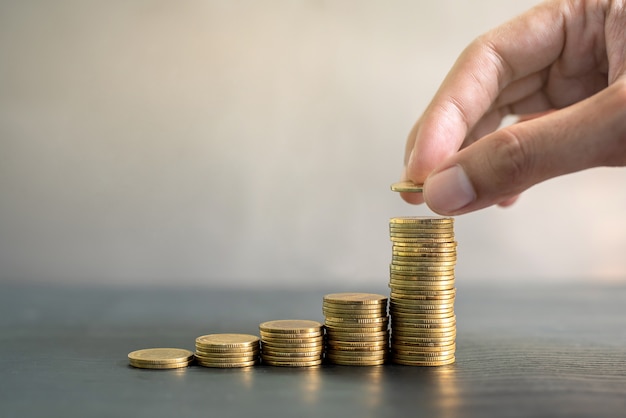 Foto mão empilhando moedas de ouro na mesa de madeira preta. negócios, finanças, marketing, conceito e design de comércio eletrônico