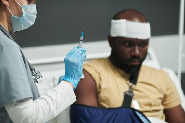 Mão enluvada de enfermeira em máscara protetora se preparando para injeção