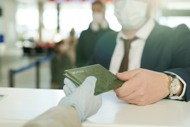 Mão enluvada de recepcionista devolvendo o passaporte do empresário elegante no balcão da recepção após o registro antes do voo