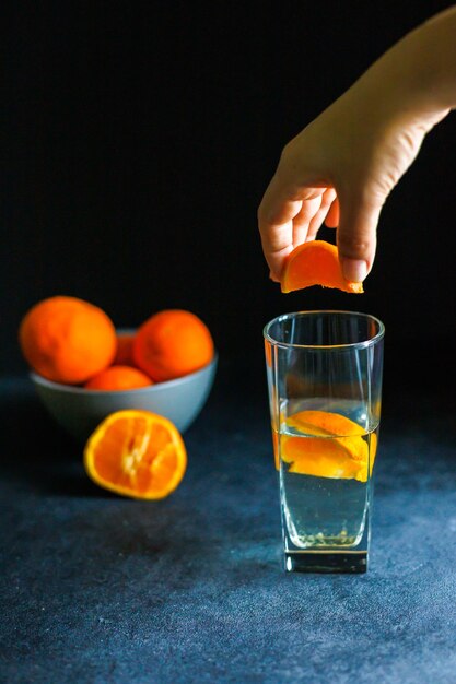 Mão espreme uma fatia de laranja em um copo de água água com suco de laranja água saudável