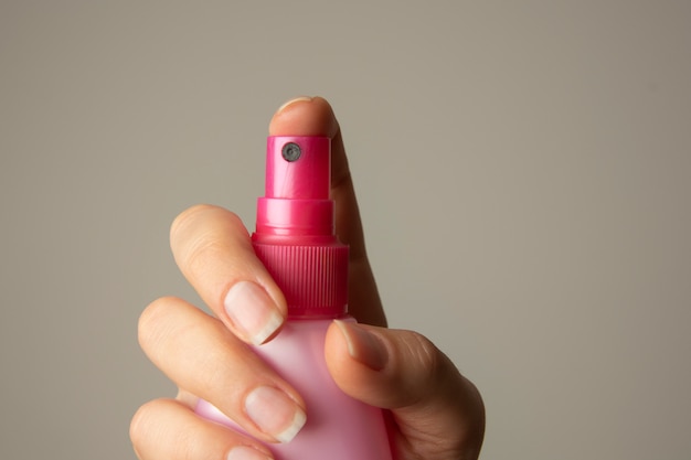 Mão fêmea que guarda o pulverizador cor-de-rosa cosmetical da garrafa, isolado. Proteção solar, cuidados com a pele.