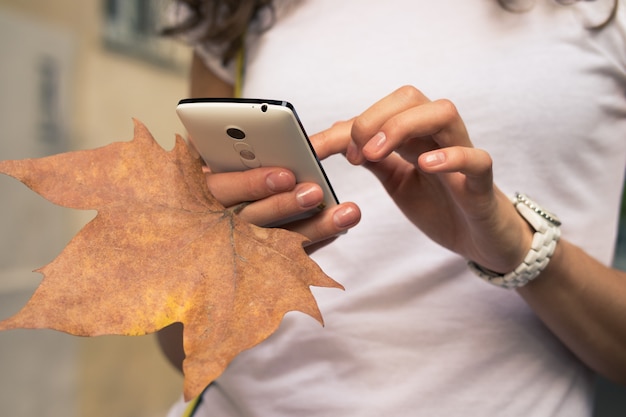 Mão fêmea que guarda um telefone celular e um close-up caído da folha.