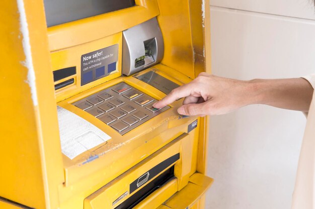 Mão feminina apertando senhas no botão do caixa eletrônico para retirar dinheiro