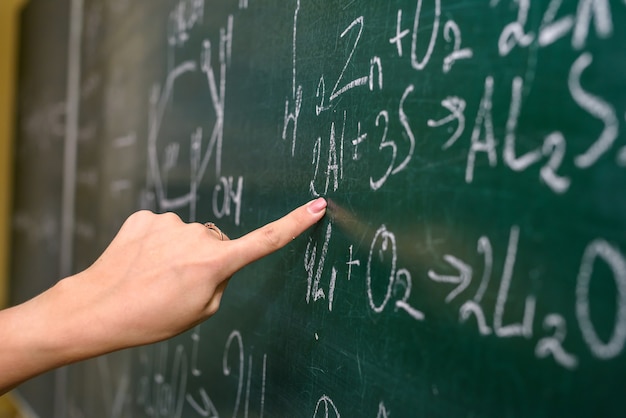 Mão feminina apontando para a fórmula química no quadro-negro close-up