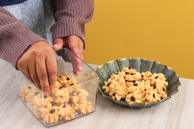 Mão feminina asiática colocar kue kering (biscoitos) na caixa transparente, preparação para venda ied mubarak kue lebaran. organize o biscoito ied na caixa. copiar espaço para texto