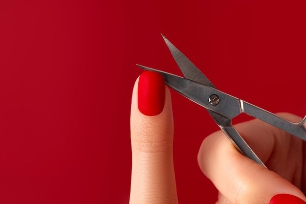 Mão feminina bem cuidada com tesoura em fundo vermelho Design de unhas vermelho fosco