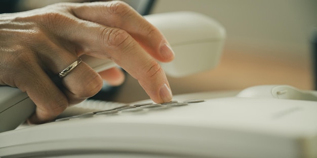 Mão feminina caucasiana segurando o receptor de telefone e discando o número de telefone