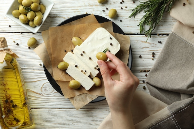 Mão feminina colocando azeitona no queijo feta, vista de cima