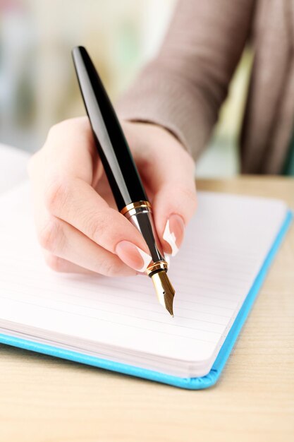 Mão feminina com caneta escrevendo no caderno closeup