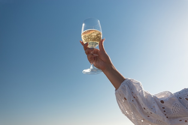 Mão feminina com copo de vinho na praia