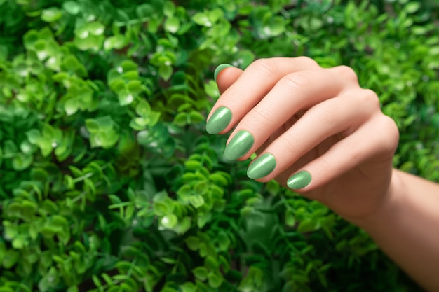 Mão feminina com design de unha verde. manicure de esmalte verde brilhante. mulher com a mão no fundo da natureza com folhas verdes