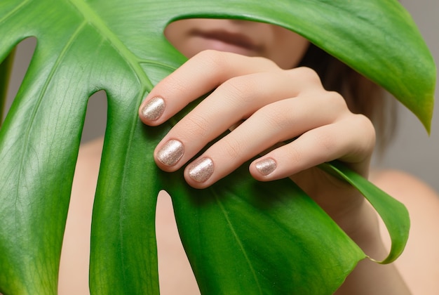 Mão feminina com design de unhas de ouro.