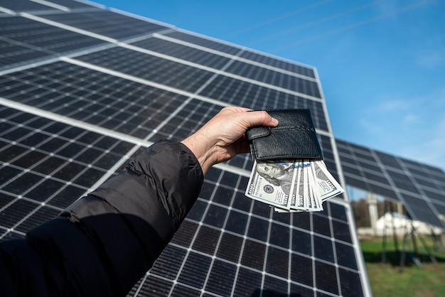 Mão feminina com dólares em uma carteira preta no fundo de painéis solares Negócios de energia solar o custo da eletricidade verde Novas tecnologias a energia do futuro