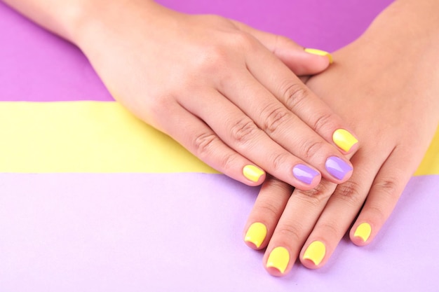 Mão feminina com elegantes unhas coloridas em fundo brilhante