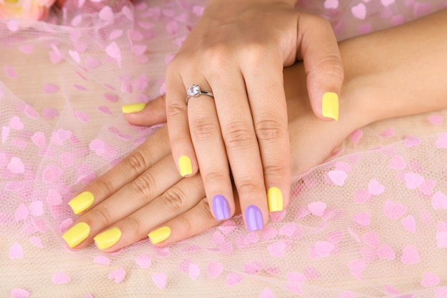 Mão feminina com elegantes unhas coloridas em fundo de tecido colorido