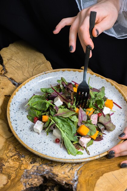 Mão feminina com garfo e salada com verduras abóbora e queijo macio