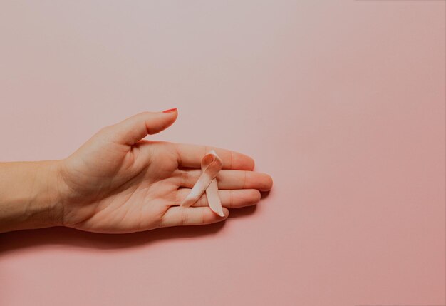 Mão feminina com laço rosa de doença de câncer em fundo rosa com fita