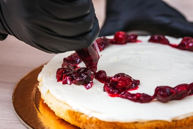 Mão feminina com luva preta espreme confitura de cereja em um cheesecake com coco