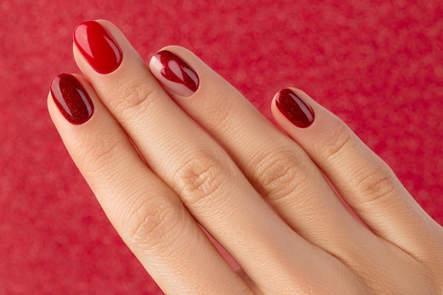 Mão feminina com manicure em fundo vermelho
