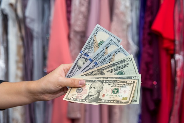 Mão feminina com notas de dólar no fundo do cabide de vestido