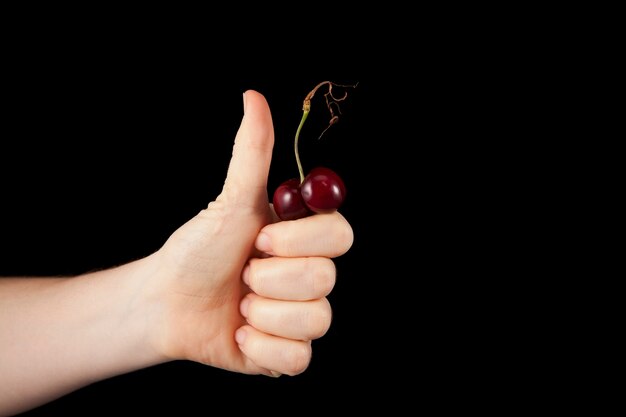 Mão feminina com o polegar para cima (como símbolo) segura uma cereja madura engraçada de forma incomum. Cerejas feias.