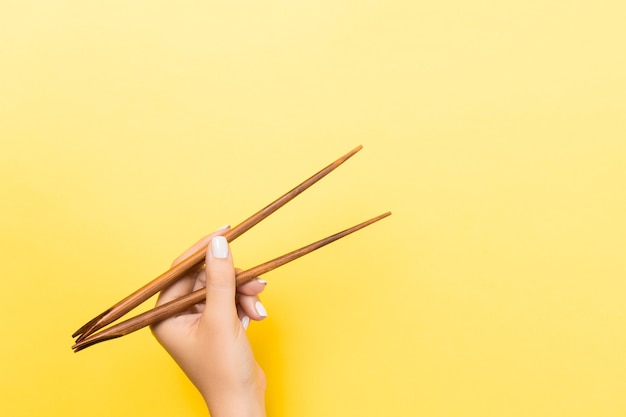 Mão feminina com pauzinhos em fundo amarelo. Comida tradicional asiática com espaço vazio para seu projeto.